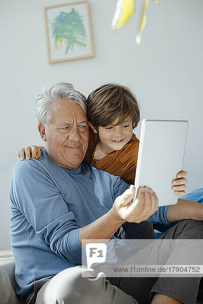 Smiling boy taking selfie with grandfather through tablet computer at home