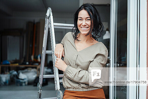 Happy woman leaning on ladder at doorway of home