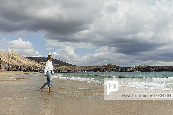 Junge Frau spaziert am Strand entlang der Küste