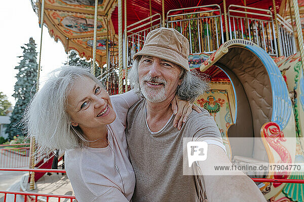 Happy man taking selfie with woman in front of carousel