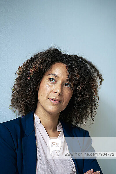 Contemplative businesswoman with curly hair in front of wall
