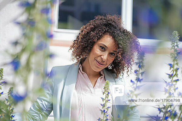 Reife Geschäftsfrau mit lockigem Haar neben Blumen