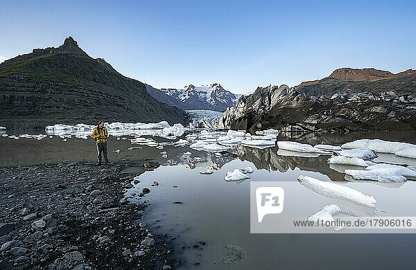 Wanderer an einem See  Spiegelung in der Gletscherlagune Svínafellslon mit Eisschollen  Gletscherzunge Svínasfellsjökull  hinten vergletscherter Berggipfel Hrútfjallstindar  bei Sonnenuntergang  Svínafell  Island  Europa