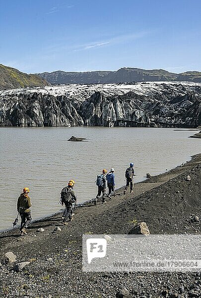 Tourists with ice axes and helmets on the lakeshore of a glacier lagoon  glacier tongue with crevasses and lake  Sólheimajökull  South Iceland  Iceland  Europe
