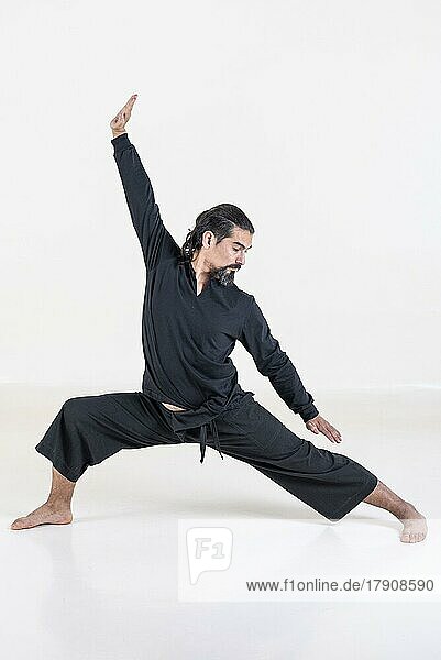 Ein schwarz gekleideter Mann macht Yoga auf weißem Hintergrund. Studioaufnahme