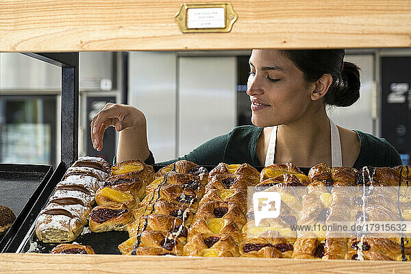 Mittlere Einstellung einer lateinamerikanischen Bäckereibesitzerin  die ihre Backwaren in einem Regal ausstellt