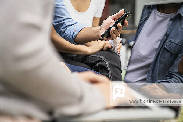 Close-up shot of young freelancers and independent contractors' hands using mobile technology to connect to network while working outdoors