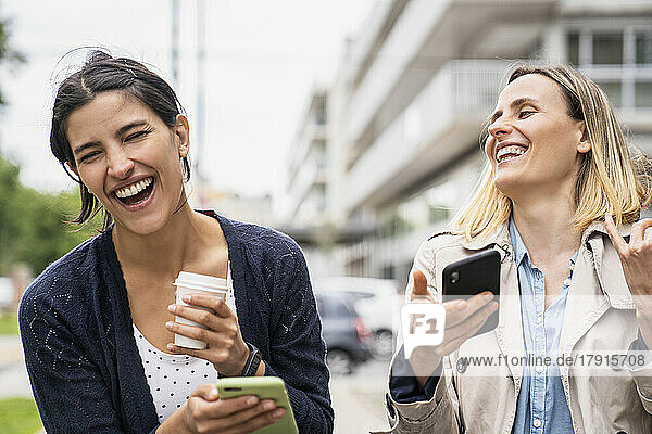 Medium shot of two female entrepreneurs laughing and enjoying content found on social media while working outdoors