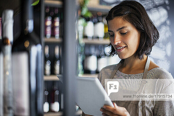 Wine store worker taking inventory of bottles on digital tablet