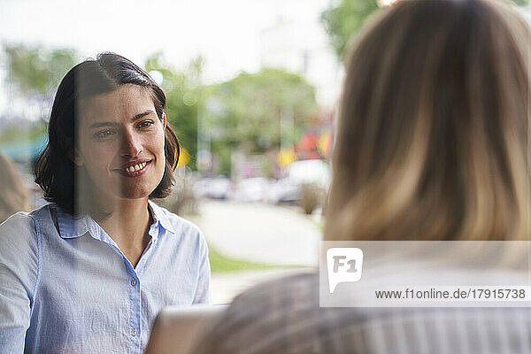 Mittelaufnahme einer lateinamerikanischen Angestellten  die mit ihrem Kollegen in einem Büro im Freien über ihre Arbeit spricht