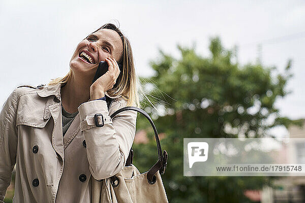 Frau lächelt und spricht mit dem Handy  während sie auf der Straße geht