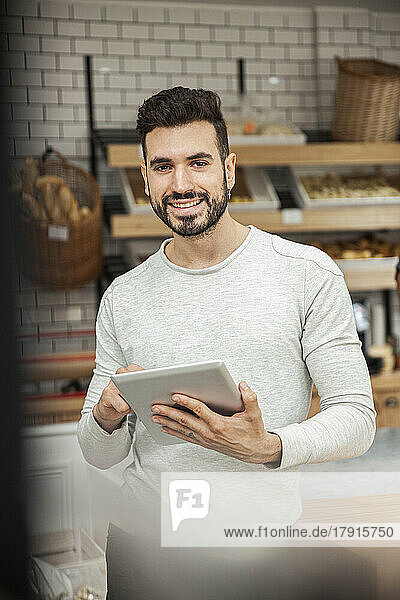 Bäckereibesitzer hält ein digitales Tablet in der Hand und blickt in die Kamera