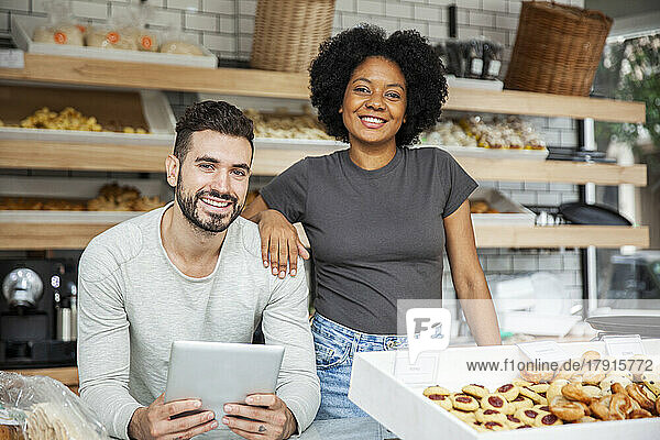 Bakery owners standing behind counter while holding digital tablet