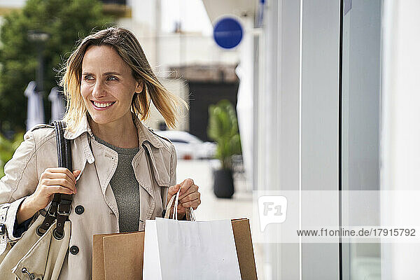 Mittelaufnahme einer lächelnden jungen Frau  die Einkaufstüten auf der Straße trägt
