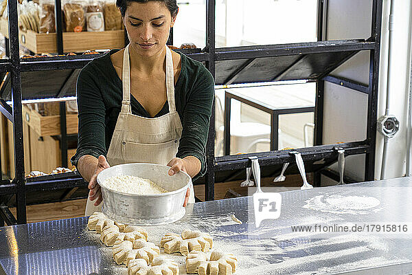 Mittlere Einstellung einer lateinamerikanischen Bäckereibesitzerin  die Mehl auf ihre Brotlaibe streut