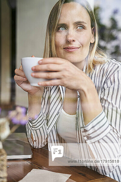 Mittelaufnahme einer attraktiven Frau  die in einem Café eine Tasse Kaffee genießt