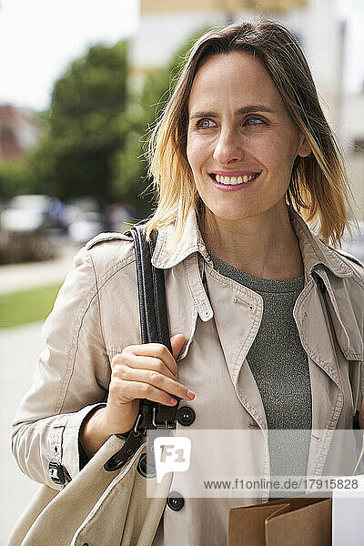 Mid-shot von lächelnden Frau hält ihre Handtasche beim Gehen auf der Straße