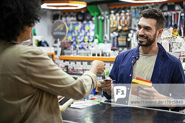 Male customer paying with credit card to African American hardware shop worker