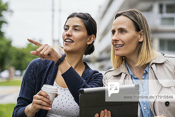 Mid-shot of two female freelance workers doing business and pointing at something while working outdoors