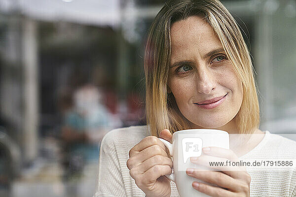 Porträt einer attraktiven Frau  die eine Tasse Kaffee in der Hand hält und den Moment genießt  in der Mitte der Aufnahme