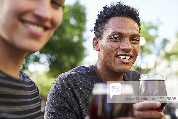 Porträt eines glücklichen jungen afroamerikanischen Mannes  der in die Kamera lächelt und ein Glas Bier hält