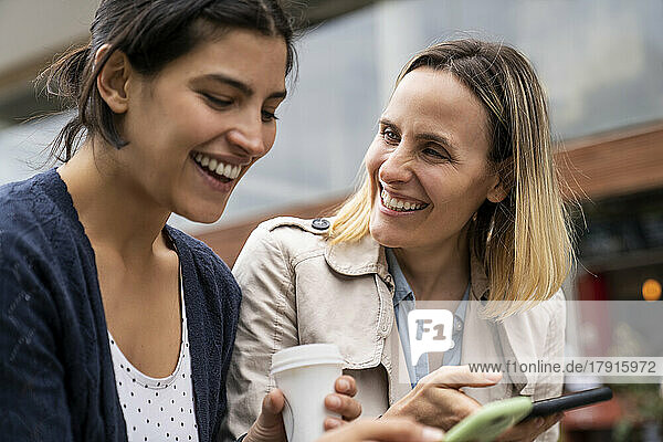 Seitenansicht von zwei Freiberuflerinnen  die im Freien arbeiten und eine gute Zeit haben  während sie ihre Smartphones überprüfen