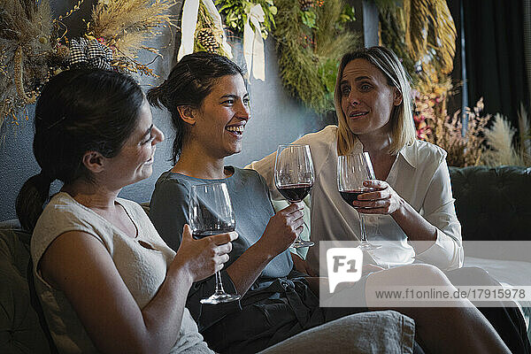 Gruppenporträt von drei fröhlichen  unterschiedlichen Freundinnen  die in einer angesagten Weinbar Wein trinken und sich unterhalten