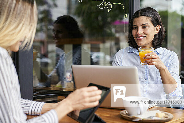 Mid-shot photo of Latin-American female entrepreneur drinking orange juice while working with her colleague