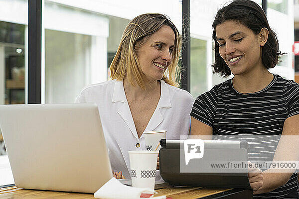Mittlere Einstellung von zwei Unternehmerinnen  die mit einem Laptop und einem digitalen Tablet arbeiten