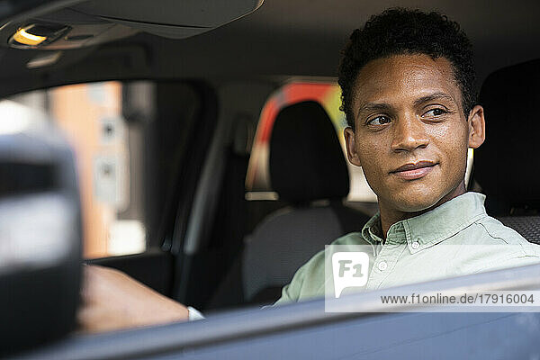 Mid-shot of handsome African-American businessman inhis car behind the wheel going to his office