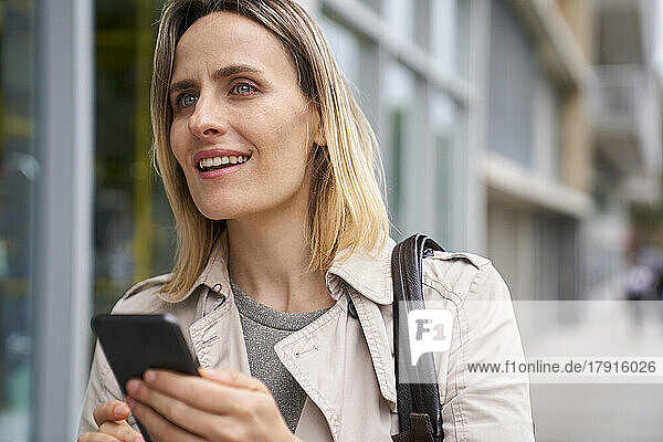 Mittelaufnahme einer attraktiven Frau  die jemanden sucht  während sie ein Handy in der Hand hält