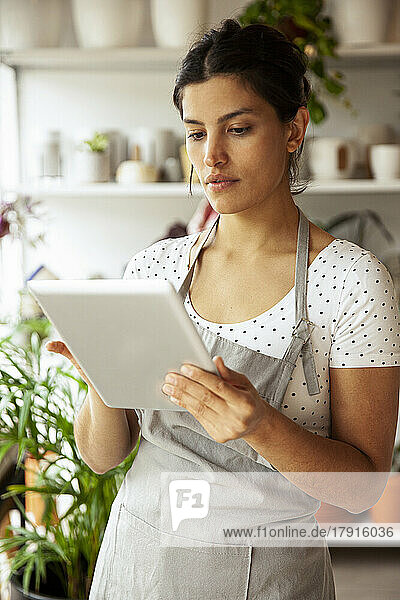 Junge erwachsene Gärtnereibesitzerin scrollt auf einem digitalen Tablet