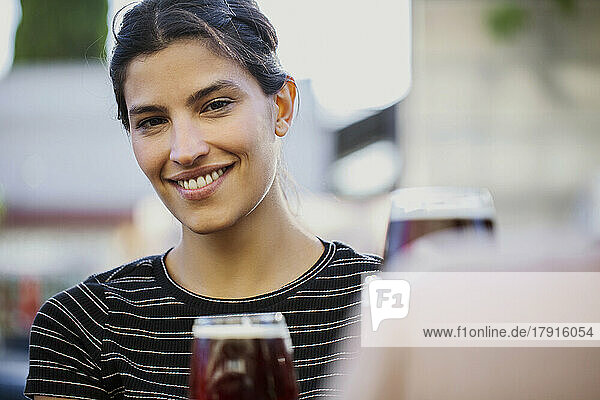 Junge Frau lächelt und schaut in die Kamera  während sie an einer Bar im Freien sitzt