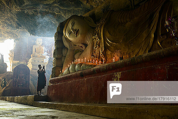 Ein Höhlentempel  eine große liegende Buddha-Statue  brennende Kerzen und ein betender Mönch.