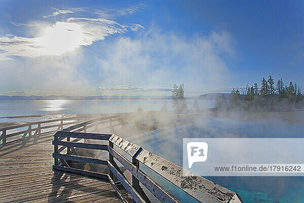 A boardwalk over water  steam rising  people in the background  and view over a lake to the mountains  in Wyoming.