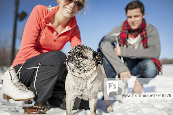 Couple kneeling in the snow with pet pug dog.