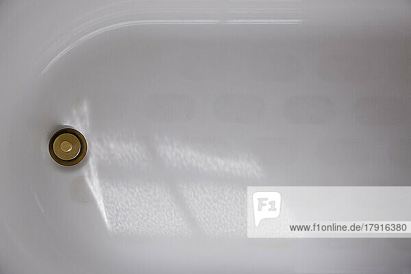 Eine Badewanne aus weißer Emaille mit einem Messingstopfen oder einem Abflussdeckel  Ansicht von oben.