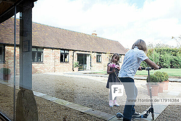 Junge und Mädchen spielen mit Roller im Hof vor dem Haus.