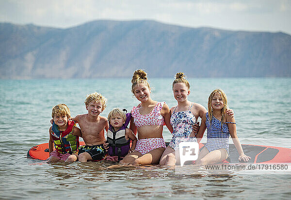 Portrait of smiling children (4-5  6-7  10-11  12-13  14-15) sitting on paddleboard on lake