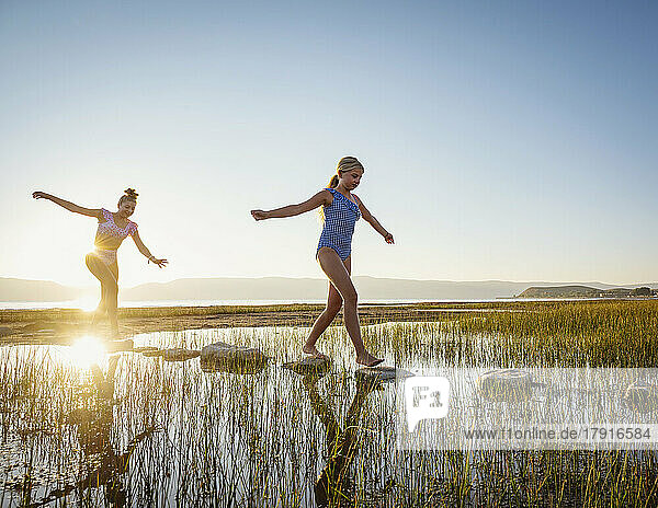 Sisters (12-13  14-15) walking on stepping stones in lake at sunrise