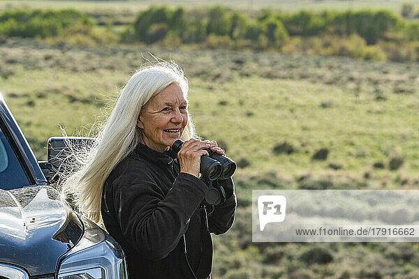 Smiling woman with binoculars at car in field