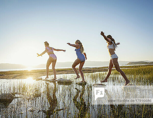 Girls (10-11  12-13  14-15) walking on stepping stones in lake at sunrise