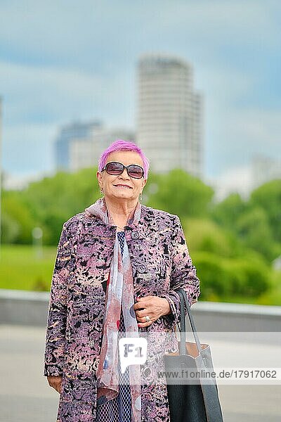 Urbanes Porträt einer fröhlichen alten Frau mit rosa Haaren und Kaschmirmantel