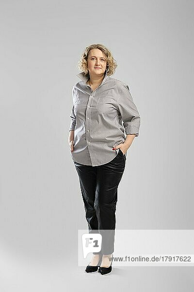 Ganzkörperporträt einer älteren Frau in grauem Hemd und Hose vor grauem Studiohintergrund