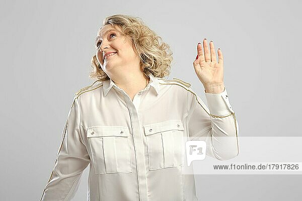 Ältere Frau winkt ungläubig mit der Hand vor grauem Hintergrund