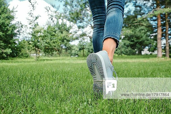 Weibliche Beine in Jeans und Turnschuhen gehen auf Gras