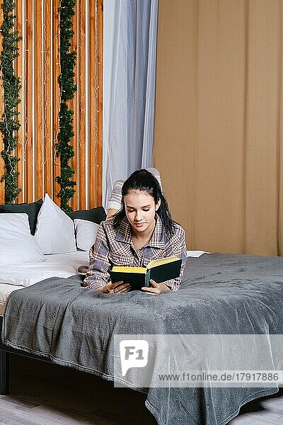 Clever young woman reading the book in bed during vacation