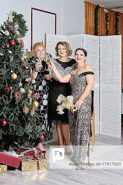 Drei fröhliche Frauen mittleren Alters  die Weihnachten in der Nähe des Weihnachtsbaums feiern