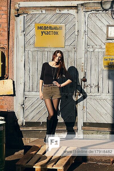 Foto eines attraktiven Mädchens  das vor einem Fabriktor mit Warnschild posiert. (Aufschrift auf dem Schild ist auf Russisch kann als Modellbereich und nicht betreten übersetzt werden)