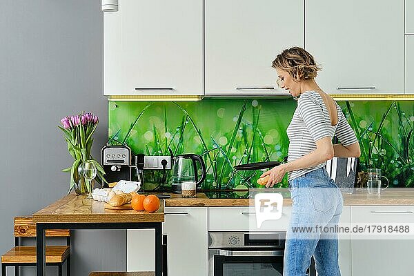 Joyful woman with frying pan in hand in the kitchen